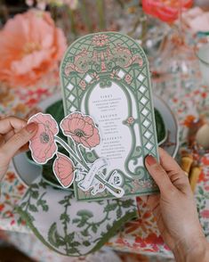 a person holding up a card on top of a table with plates and flowers in the background