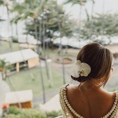 a woman with a flower in her hair looking out the window at an ocean and palm trees