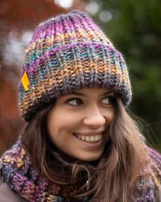 a smiling woman wearing a multicolored knitted hat with a yellow tag on it