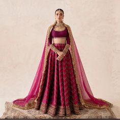 a woman in a red and gold lehenga with her hands on her hips