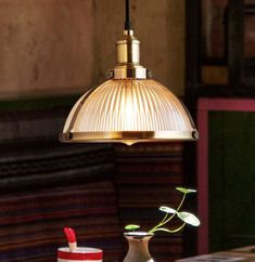 a lamp hanging over a table next to a vase with a flower in it and two cups on the table