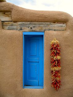 a blue door and window with red peppers hanging from it's side, in front of a adobe - style building