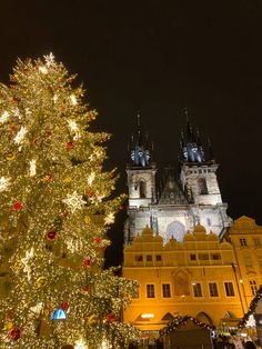 a large christmas tree in front of a building with lights on it's sides