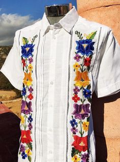 PRESIDENT STYLE GUAYABERA CLASSIC & AUTHENTIC ELEGANT PRESIDENT STYLE GUAYABERA 100% LINEN White color Feature beautiful and unique vibrant colorful floral embroidery, (double) 100 % Linen 1 back panel. Short Sleeve Button-down Dress Shirt Made in Mexico A Beautiful Guayabera for any occasion! Care instructions: This beautiful item was handmade. To maintain the quality of the work, we highly recommend dry clean. Or hand wash in cold water with mild soap, and air drying. Quinceanera Ideas Mexican, Mexican Theme Party Outfit, Latin Inspired Wedding, Outfit Mexicano, Mexican Inspired Wedding, Wedding Fiesta, Mexican Themed Weddings, Hacienda Wedding, Mexican Wedding Dress