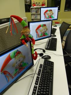 two computer monitors with elf dolls on them sitting in front of the keyboard and mouse