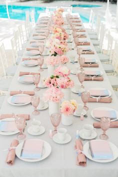 a long table set up with pink and white plates, napkins and flowers in vases