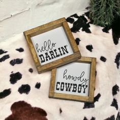 two wooden framed signs sitting on top of a cow print rug with the words hello darlin, happy cowboy