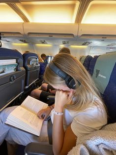 a woman sitting in an airplane reading a book and wearing headphones on her ears