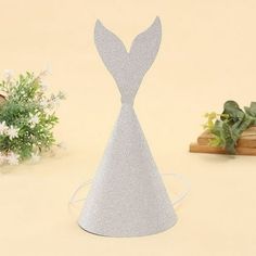 a silver glittered paper hat shaped like a mermaid tail on a table next to flowers