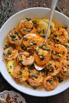 a white bowl filled with cooked shrimp and capers on top of a wooden table