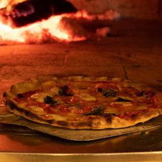 a pizza sitting on top of a metal pan in front of an open fire oven