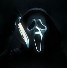 a man in a hooded jacket holding a knife and wearing a ghost mask with his mouth open