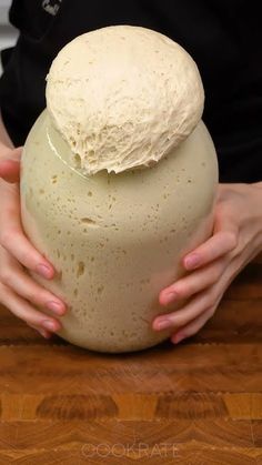 a person holding a large round object on top of a wooden table with their hands