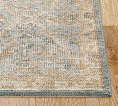 a beige and blue area rug on the floor with wood floors in front of it