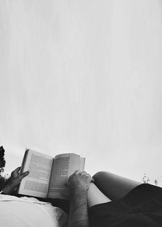 a man laying on top of a bed holding an open book in his hand and reading it