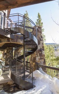 a spiral staircase in front of a stone building with snow on the ground and trees around it