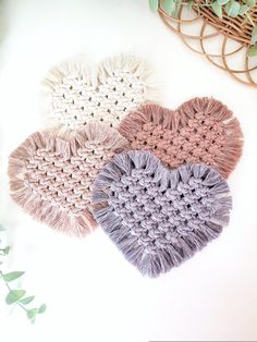 three crocheted heart shaped doily on a white surface with greenery in the background