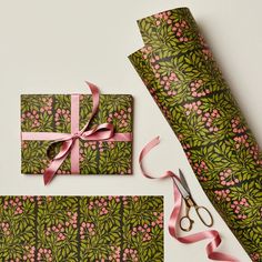 wrapping paper with pink flowers and green leaves on it next to a pair of scissors