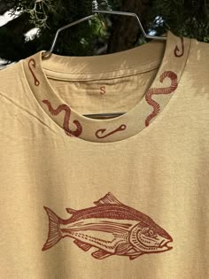 Printed with hand carved linocut/block print stamps. Each piece is unique and imperfect and printed at my home studio in Los Angeles. No digital printing or drop shipping here!  This shirt features a salmon as its main design on the front of the shirt in maroon. It also features a collar and sleeve detail front and back with hooks and worms encircling:) 100% Heavyweight Cotton Tee Shirt  Unisex Sizing (runs a bit small) Machine Washable. Line dry for longevity of vibrancy or on low heat. Please