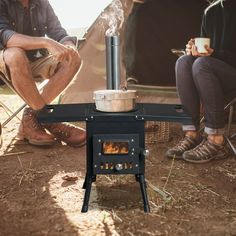 two people sitting in front of an outdoor stove with a cup of coffee on it