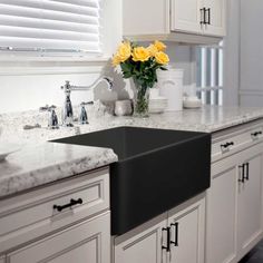 a kitchen with white cabinets and yellow flowers in the vase on the sink countertop