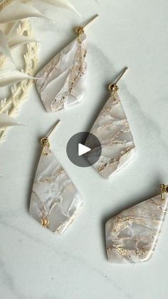 three pieces of jewelry sitting on top of a white table next to some feathers and flowers