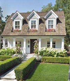 a white house with lots of windows and flowers in the front yard, surrounded by greenery