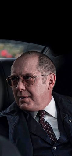 an older man in a suit and tie sitting in a car with his head turned to the side