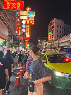 many people are walking down the street in front of cars and neon signs at night