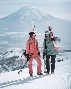 two people standing on top of a snow covered slope with skis in their hands