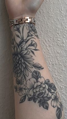 a woman's arm with black and white flowers on it, in front of a wall