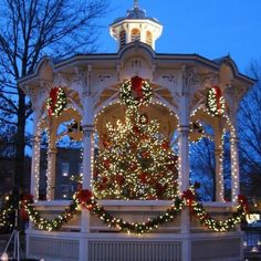 a white gazebo with christmas lights and a lit up tree in the front yard