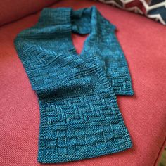 two knitted scarves sitting on top of a red couch