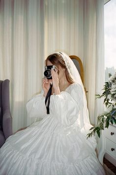 a woman in a wedding dress is taking a picture with her camera while sitting on a chair