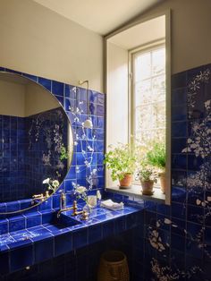 a blue tiled bathroom with potted plants on the window sill and a round mirror