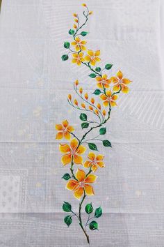 a white table cloth with yellow flowers on it and green leaves painted on the side