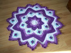 a purple and white crocheted blanket on the floor