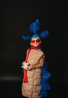 a person in a costume holding a cup and saucer with blue feathers on it