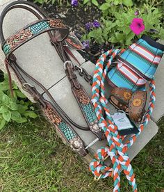 a horse bridle, reins and rope on the ground in front of some flowers