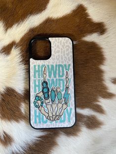 a cell phone case sitting on top of a cowhide pattern with the words howdy hooray