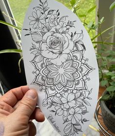 a person holding up a piece of paper with an intricate flower design on the side