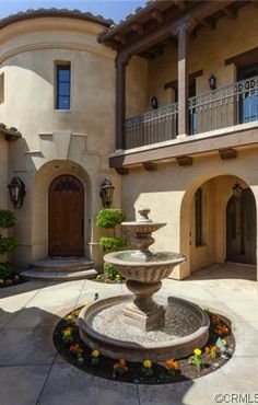 a large house with a fountain in the middle of the front yard and landscaping around it