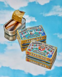 three tins of food sitting on top of a blue and white background with clouds