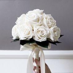 a bouquet of white roses is held by someone's hand in front of a gray wall