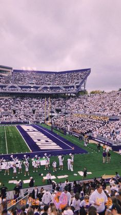 a football stadium filled with fans and players on the sidelines during a cloudy day