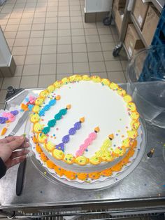 a person is decorating a birthday cake with colorful icing on a table in a kitchen