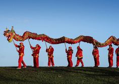 a group of people dressed in red and yellow holding a dragon shaped kite on top of a hill