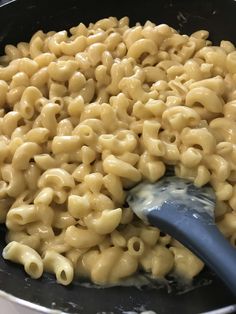 macaroni and cheese is being cooked in a pan with a blue spatula