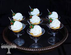 cupcakes with white frosting and holly decorations are on a glass platter