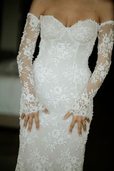 a woman in a white wedding dress with long sleeves and lace on her arms is posing for the camera